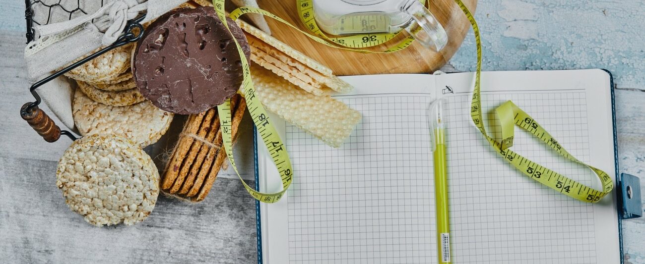 A notebook and a tape measure beside biscuits and a jar of water