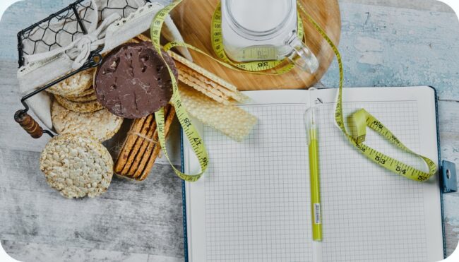 A notebook and a tape measure beside biscuits and a jar of water